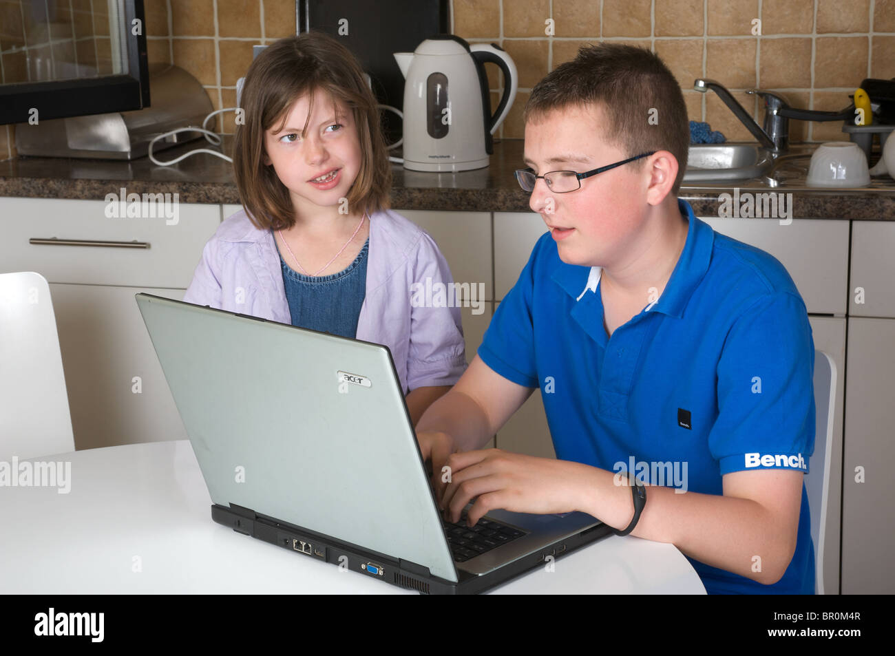Jüngere Schwester, die gerade ihr Bruder seine Schule Hausaufgaben auf seinem Laptopcomputer Stockfoto