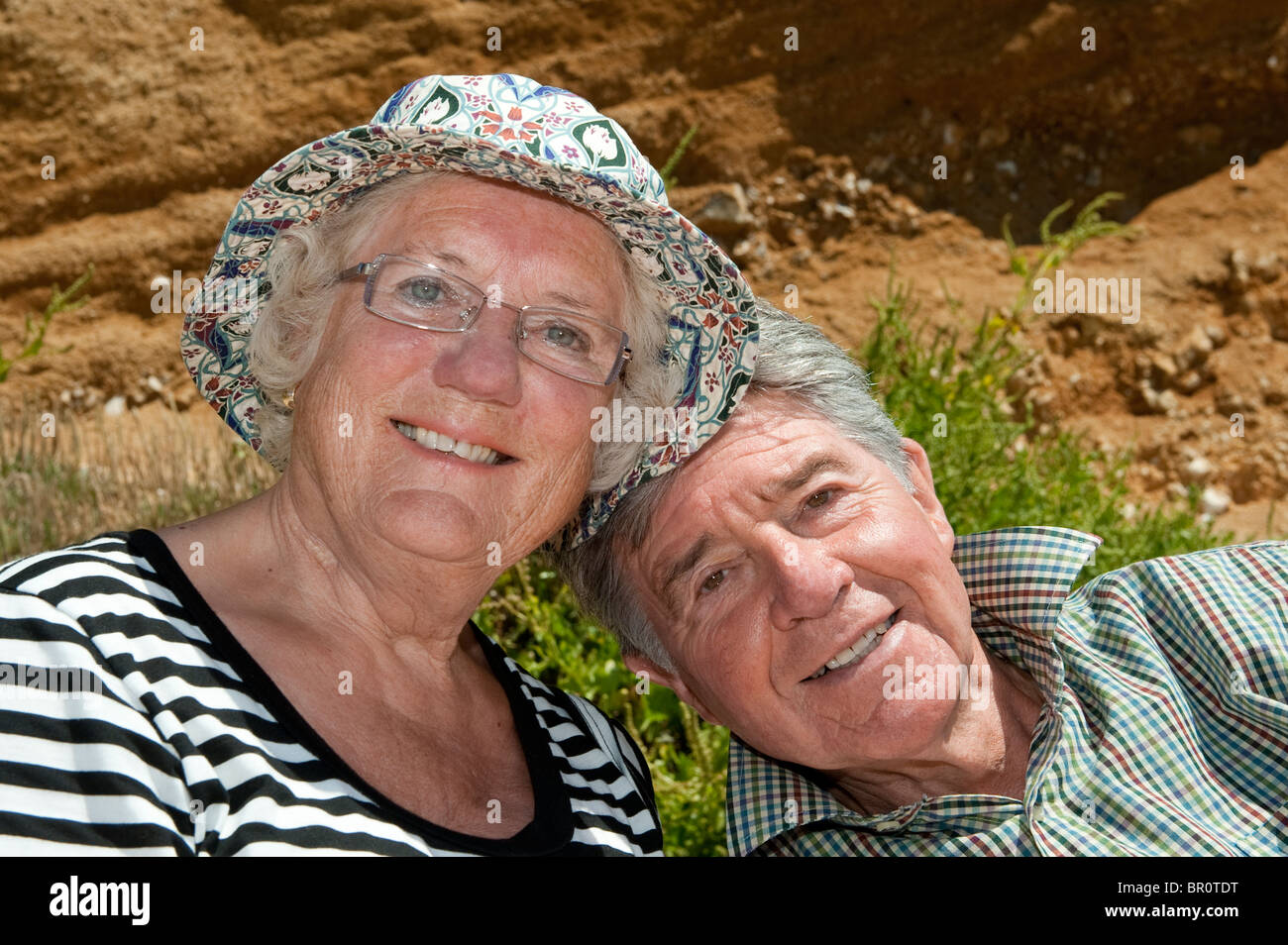 Älteres Ehepaar draußen sitzen auf einem Sommer Tag Lächeln. Stockfoto
