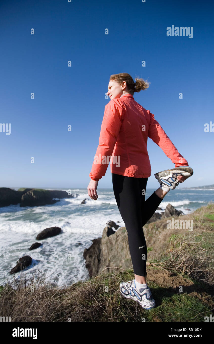 Junge Frau in roten Jacke erstreckt sich vor einem Lauf an der Küste, Nord-Kalifornien. Stockfoto