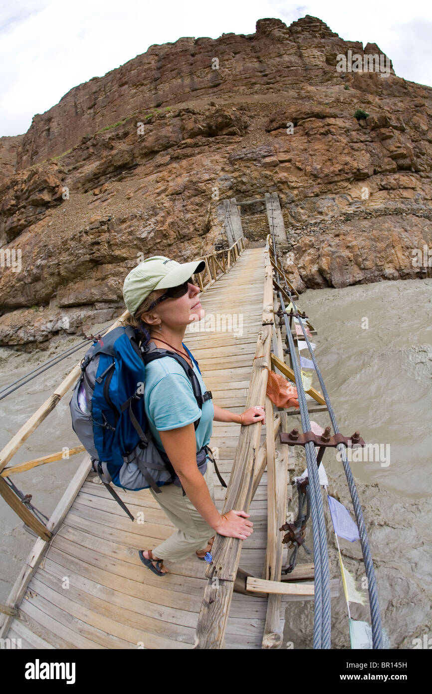Frau mit Rucksack steht auf hölzerne Brücke über den Fluss in der Nähe von Phuktal Kloster in Zanskar robust, hohe Höhe Bergen in n Stockfoto
