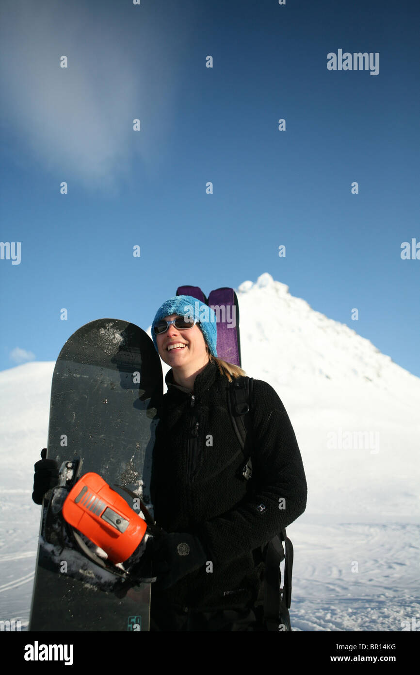 Schöne junge Frau mit Snowboard am Fuße des Berges. Stockfoto