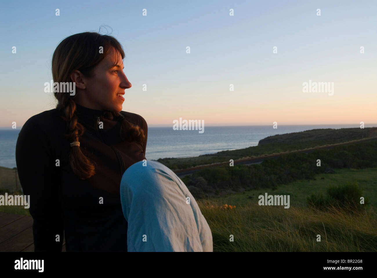 Eine Frau Yong beobachtet den Sonnenuntergang von einem Deck mit Blick auf den Pazifischen Ozean in Hollister Ranch, California. Stockfoto