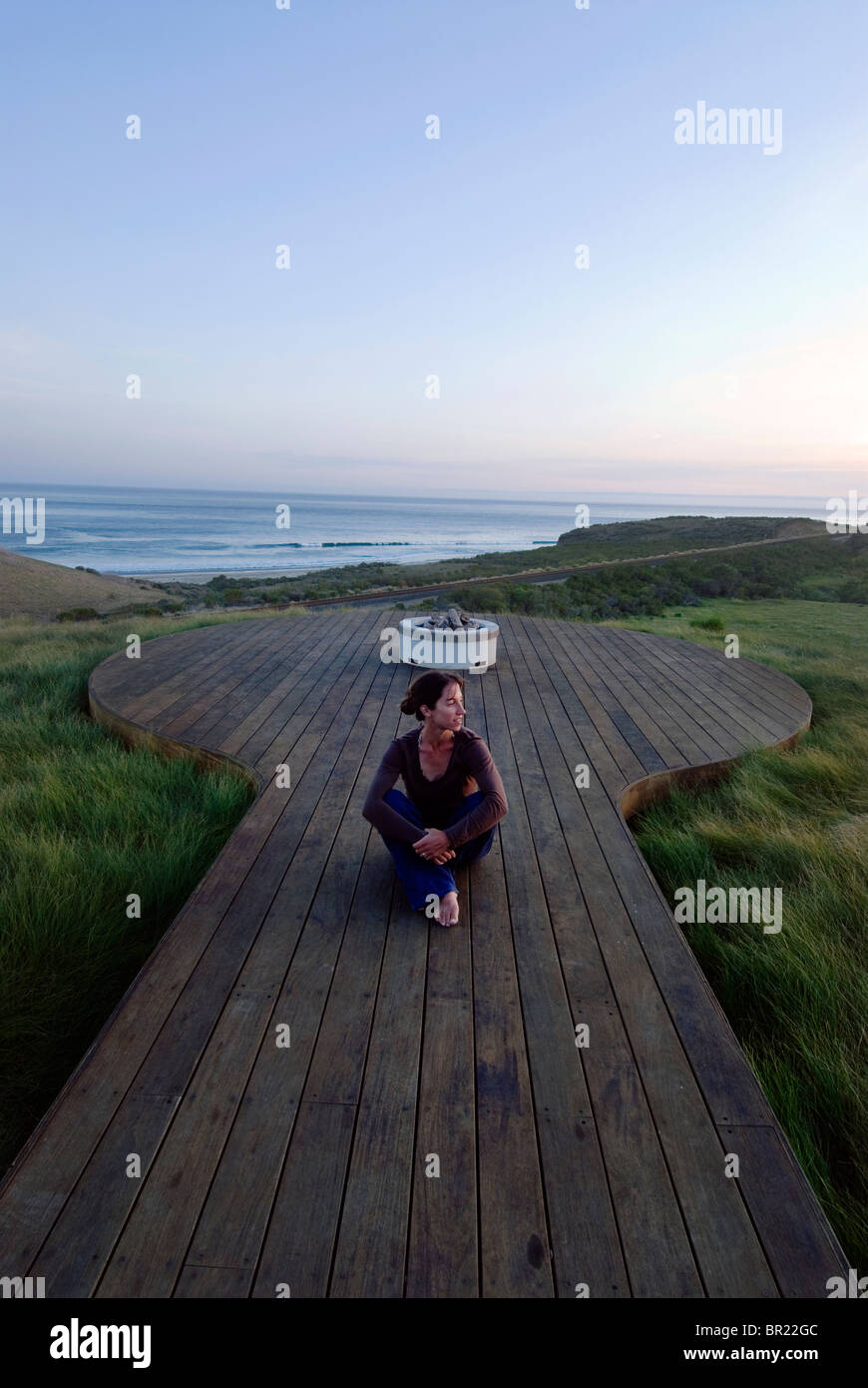 Eine Frau Yong beobachtet den Sonnenuntergang von einem Deck mit Blick auf den Pazifischen Ozean in Hollister Ranch, California. Stockfoto