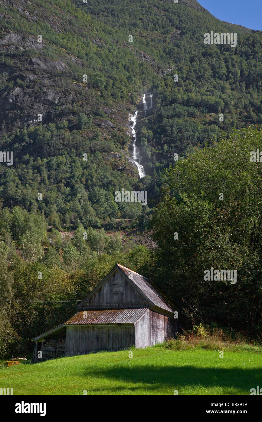 Ein Wasserfall im Tal Olden, Norwegen, landwirtschaftliche Gebäude im Vordergrund, hellem Sonnenlicht Stockfoto