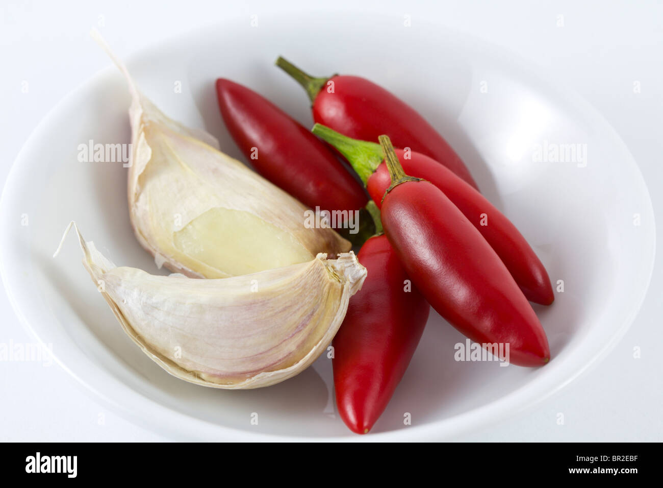 Rote Chilis und lila Knoblauch in einer weißen Schüssel auf weißem Hintergrund Stockfoto