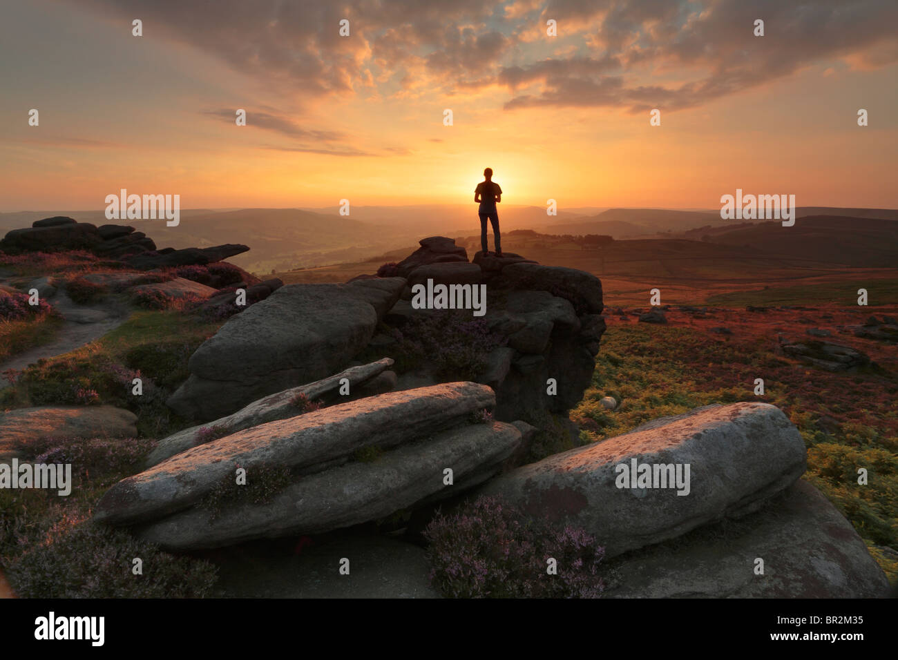 Silhouette einer Frau steht auf einem Felsvorsprung von Owler Tor in der Nähe von Hathersage im Peak District von Derbyshire, England. Stockfoto
