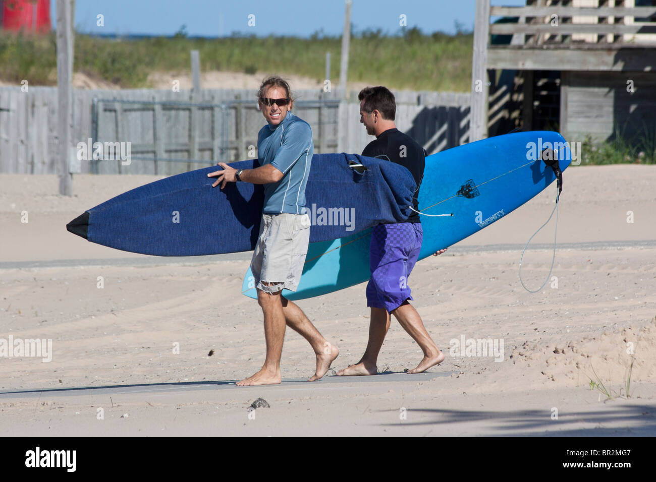 Zwei junge amerikanische Sportsurfer mit Surfbrettern, die am Sandstrand des Lake Michigan an der Küste von MI entlang spazieren Stockfoto