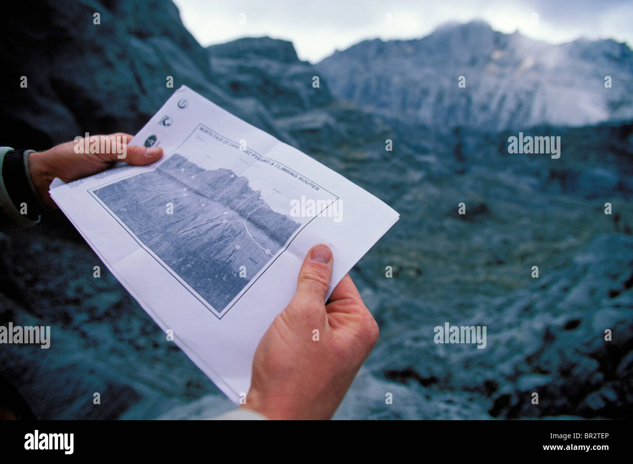 Hände halten eine Topo-Karte von Kletterrouten auf einem Berg im Hintergrund. Stockfoto