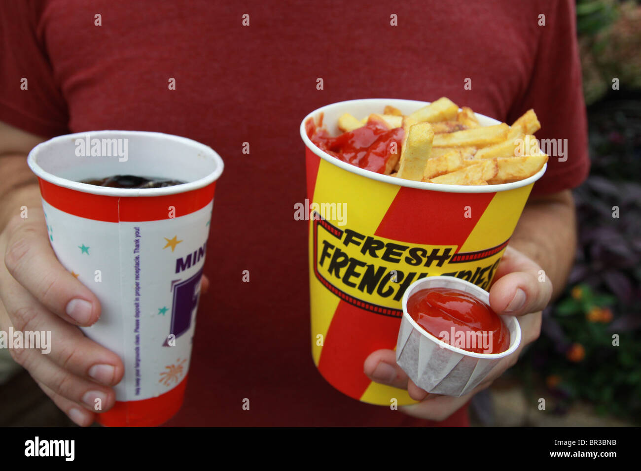 Eine Person, die einen großen Behälter mit Pommes frites, Ketchup und Soda. Stockfoto