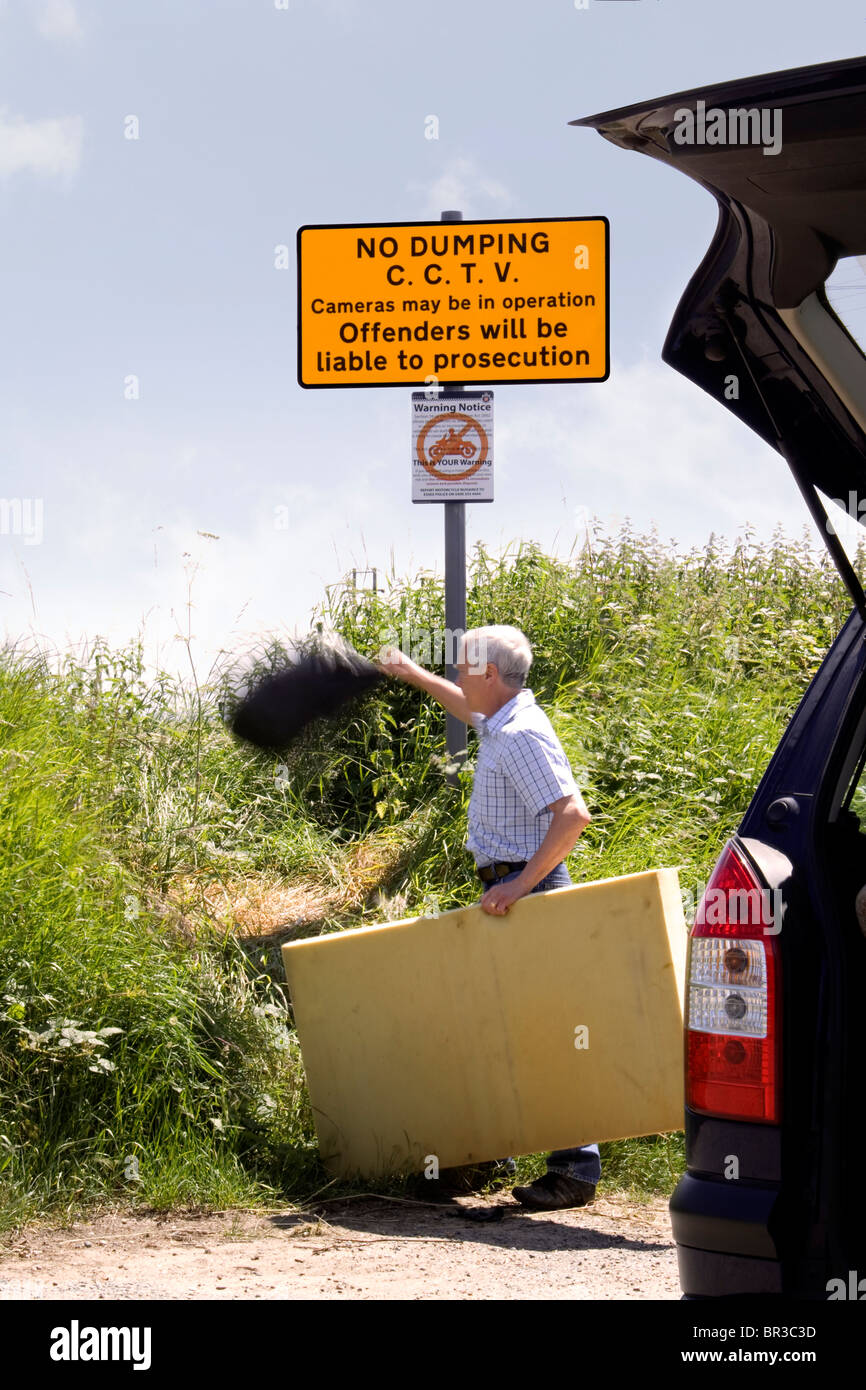 Ein Mann wirft einem Beutel mit Müll in einen Feldweg unter einem "kein dumping" Zeichen welche Zustände, die CCTV-Kameras in Betrieb sind Stockfoto