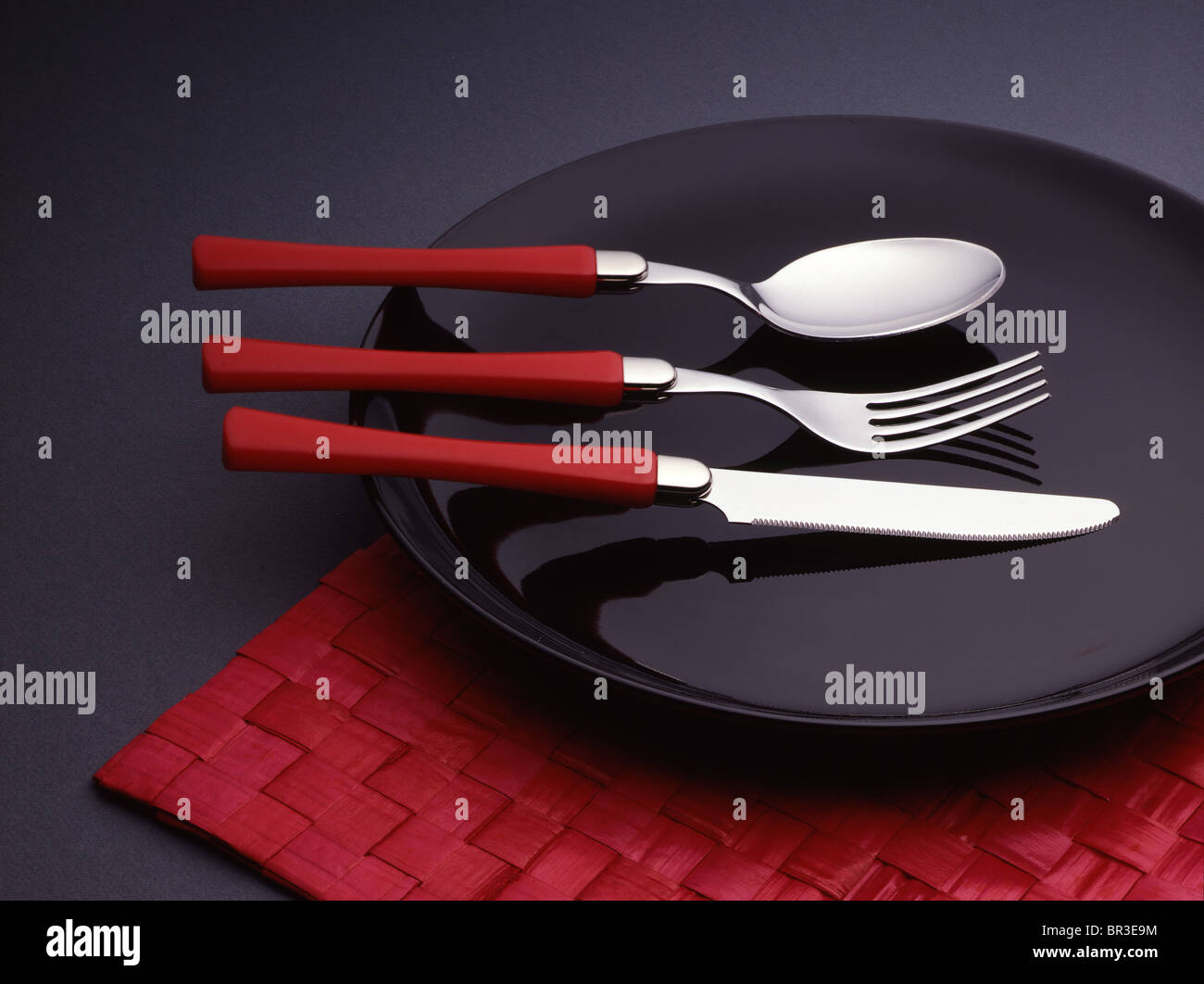 Löffel, Gabel und Messer auf einem schwarzen Teller. Stockfoto