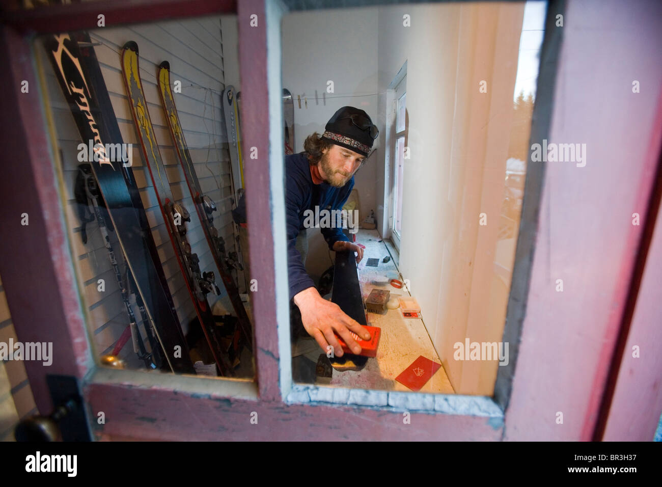 Skifahrer Will Wacker tunes Ski hinter Fenster auf Veranda in Haines, Alaska (Weitwinkel). Stockfoto