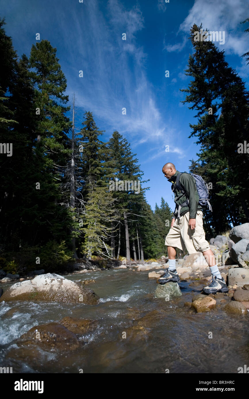 Afrikanische amerikanischer Mann, Amor Alexander geht auf Felsen während der Überfahrt Stream in den Cascade Mountains, Oregon. Stockfoto