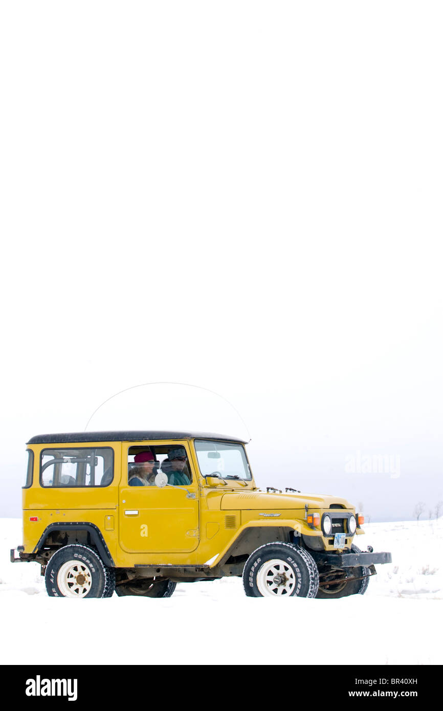 Zwei junge Frauen fahren einen alten gelben Landcruiser im Schnee in Jackson, Wyoming Stockfoto