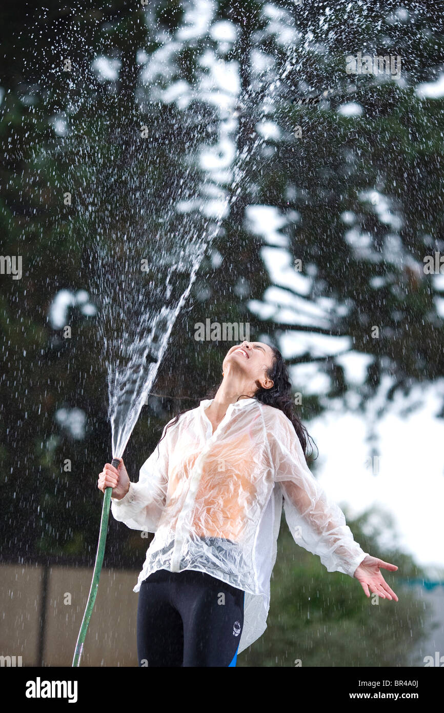 Eine Dame in Regenjacke sprüht Schlauch auf sich selbst, San Diego, Kalifornien. Stockfoto