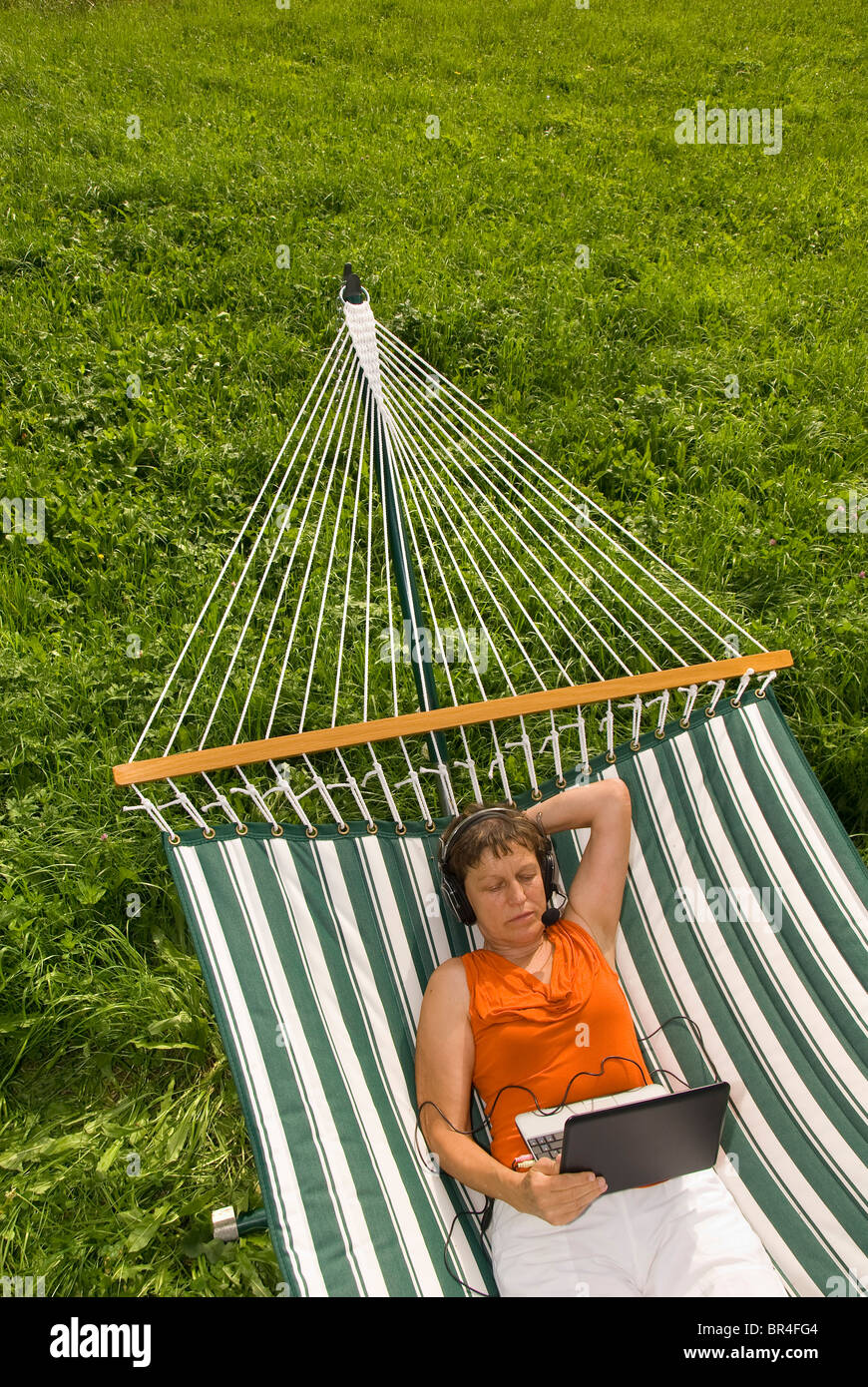 Ältere Frau mit Netbook und Kopfhörer liegen in der Hängematte Stockfoto