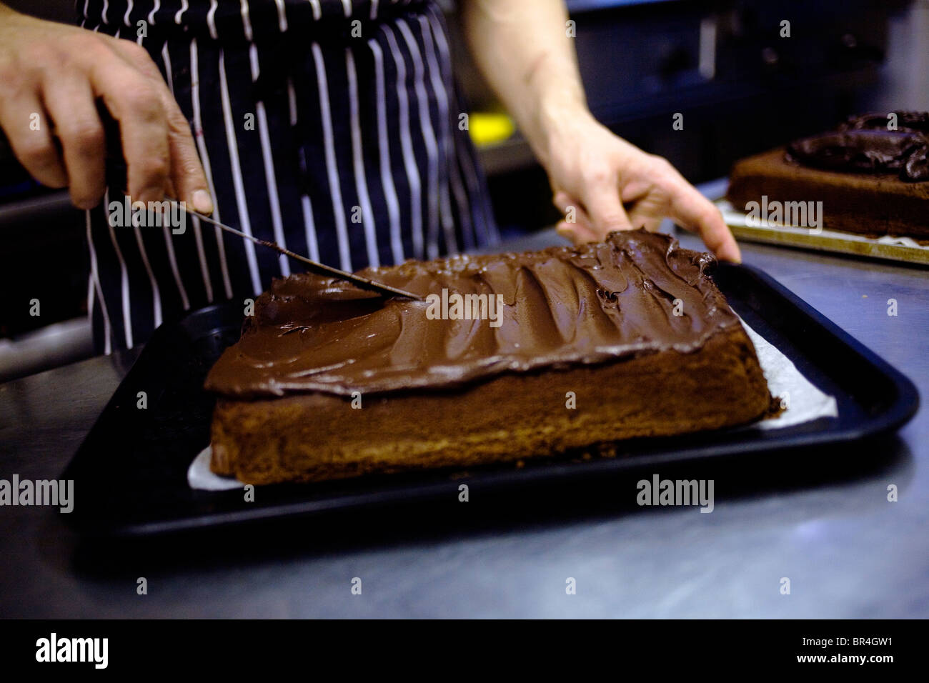 Ein Koch geben seine Schokoladenbrownie eine Schokoladenglasur. Stockfoto