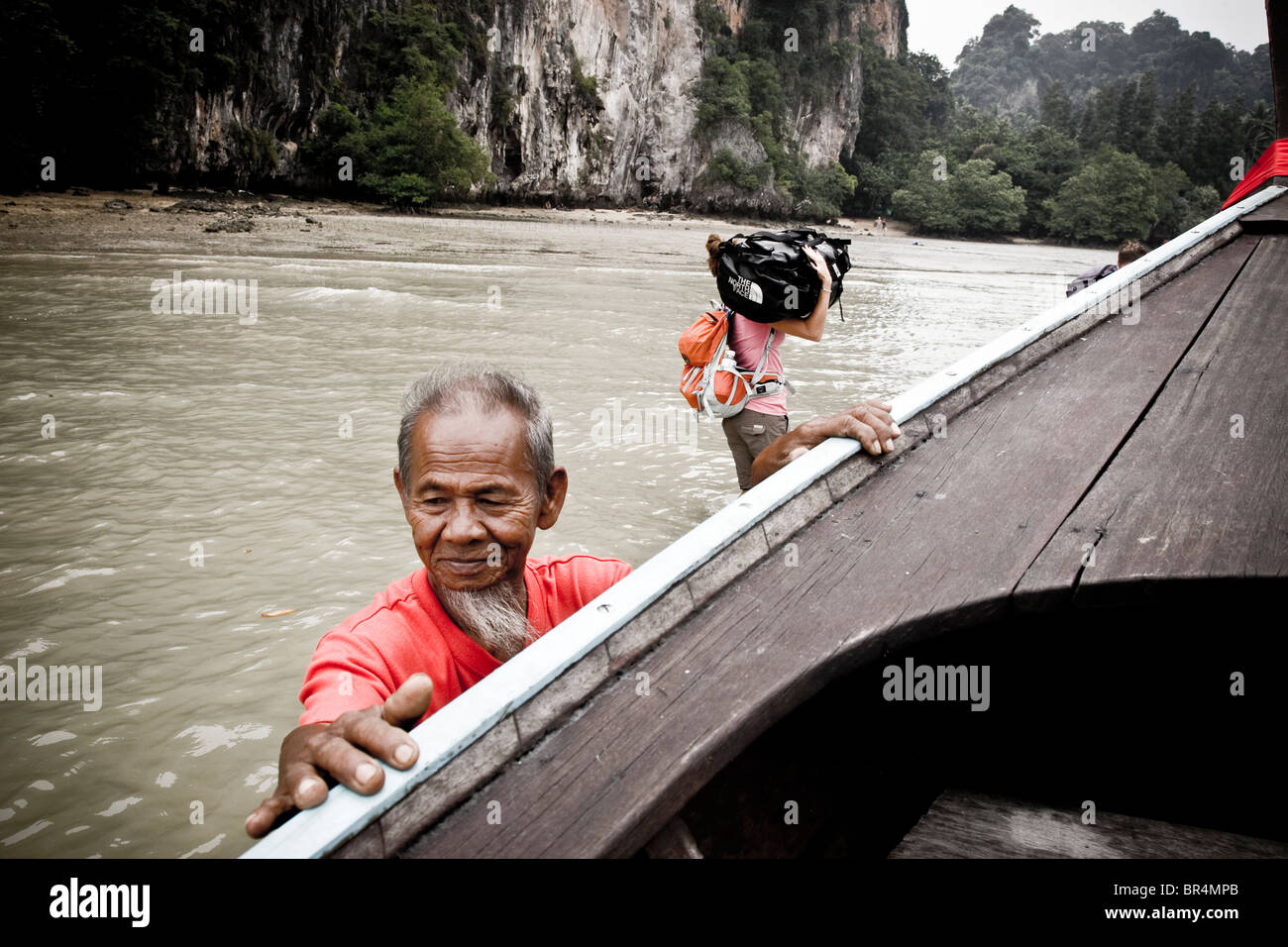 Ein Mann, der sein Boot zu tieferem Wasser als Passagiere in Richtung Ufer in waten herausschieben Stockfoto
