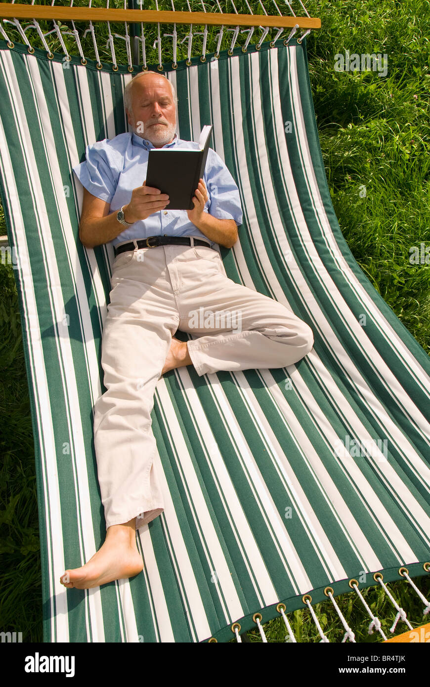 Älterer Herr liegen in der Hängematte, ein Buch zu lesen Stockfoto