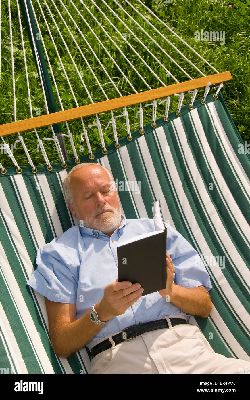 Älterer Herr liegen in der Hängematte, ein Buch zu lesen Stockfoto