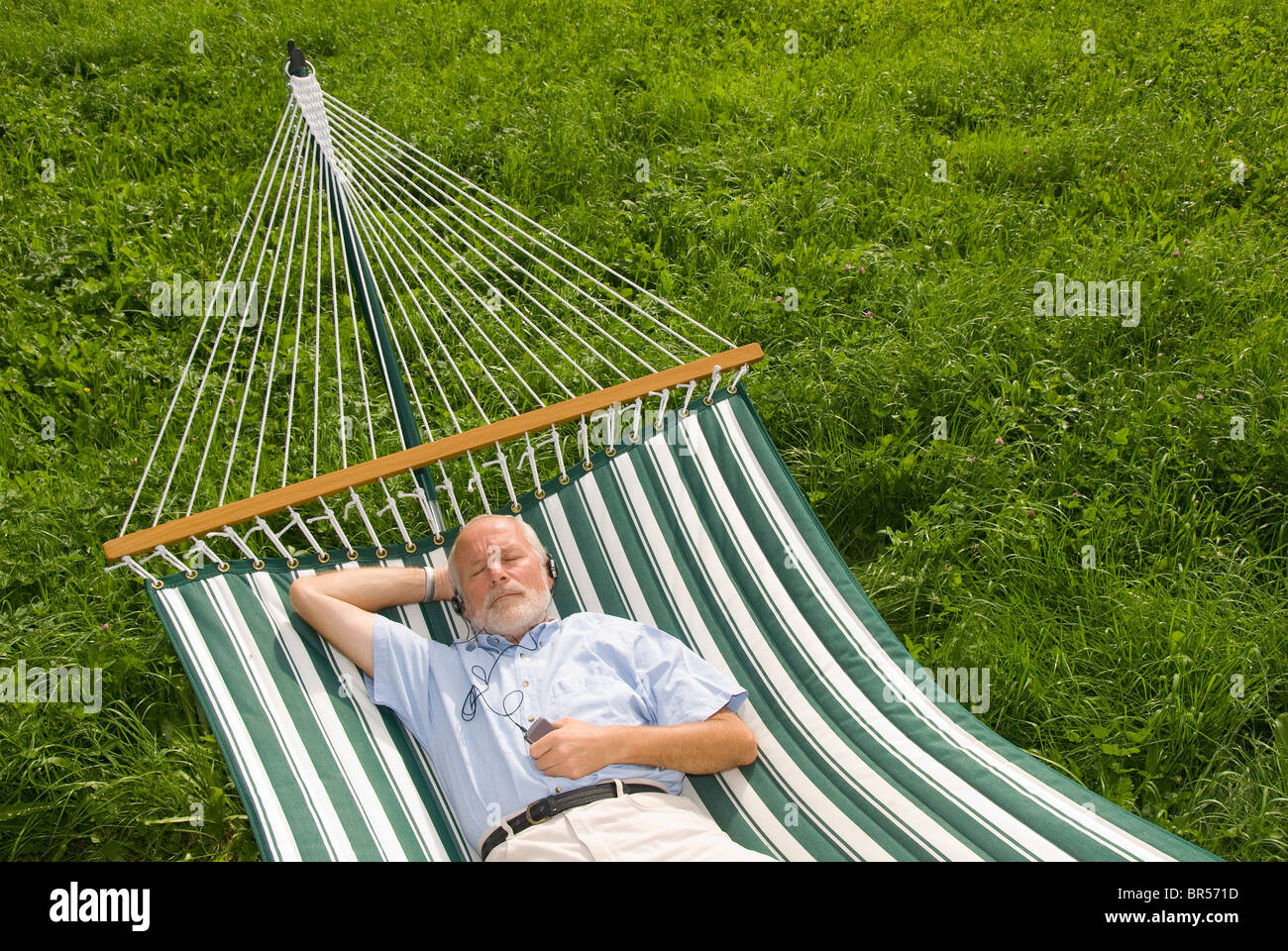 Älterer Herr liegen in der Hängematte und Musik hören Stockfoto