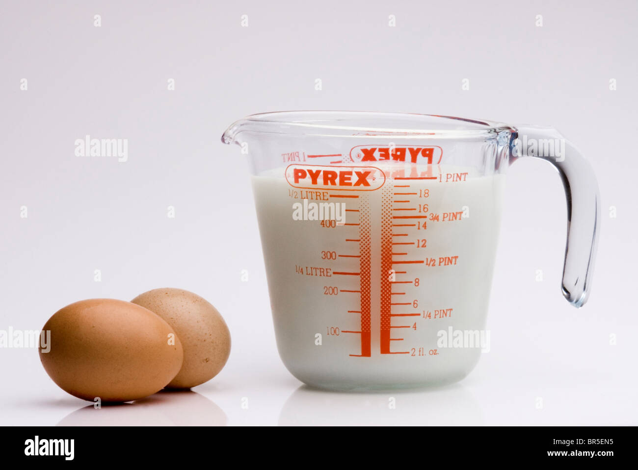 Krug mit Milch und zwei Eiern auf weiß. Stockfoto