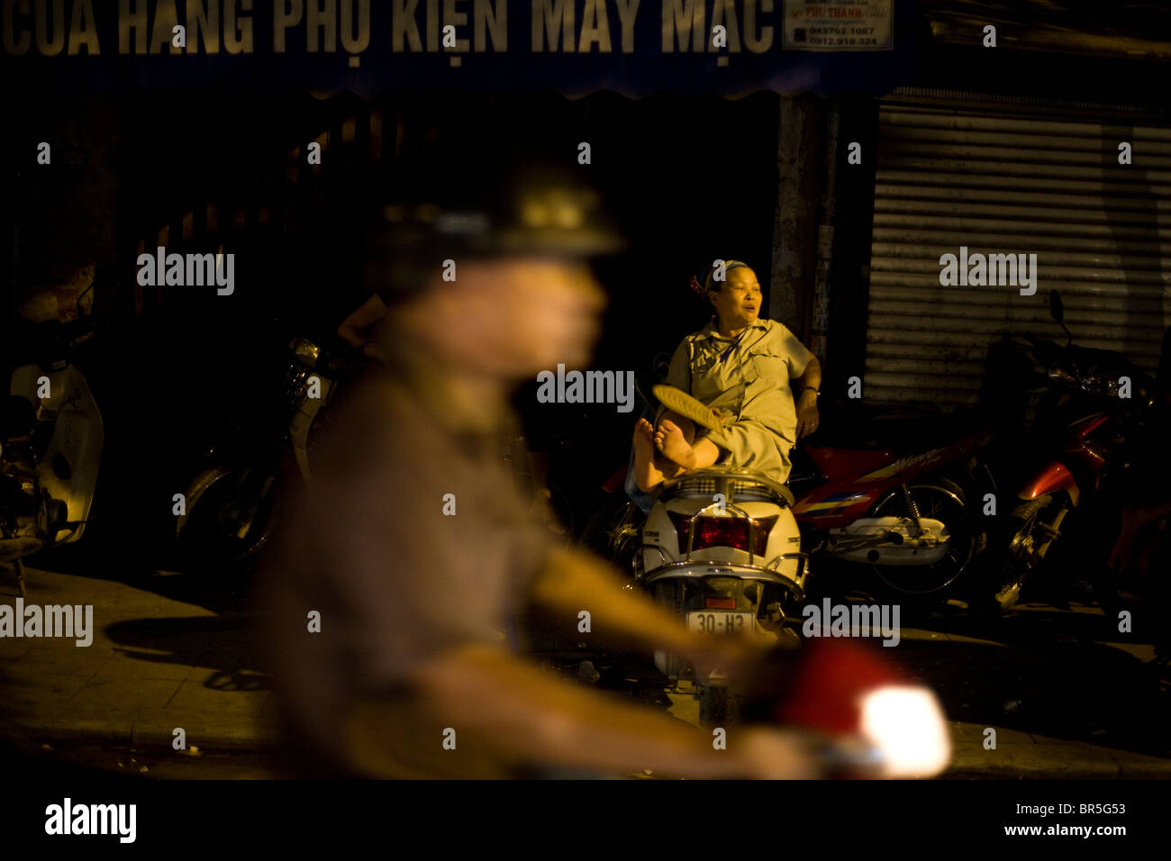 Frau ruht auf dem Motorrad als Soldat fährt vorbei, Hanoi, Vietnam Stockfoto