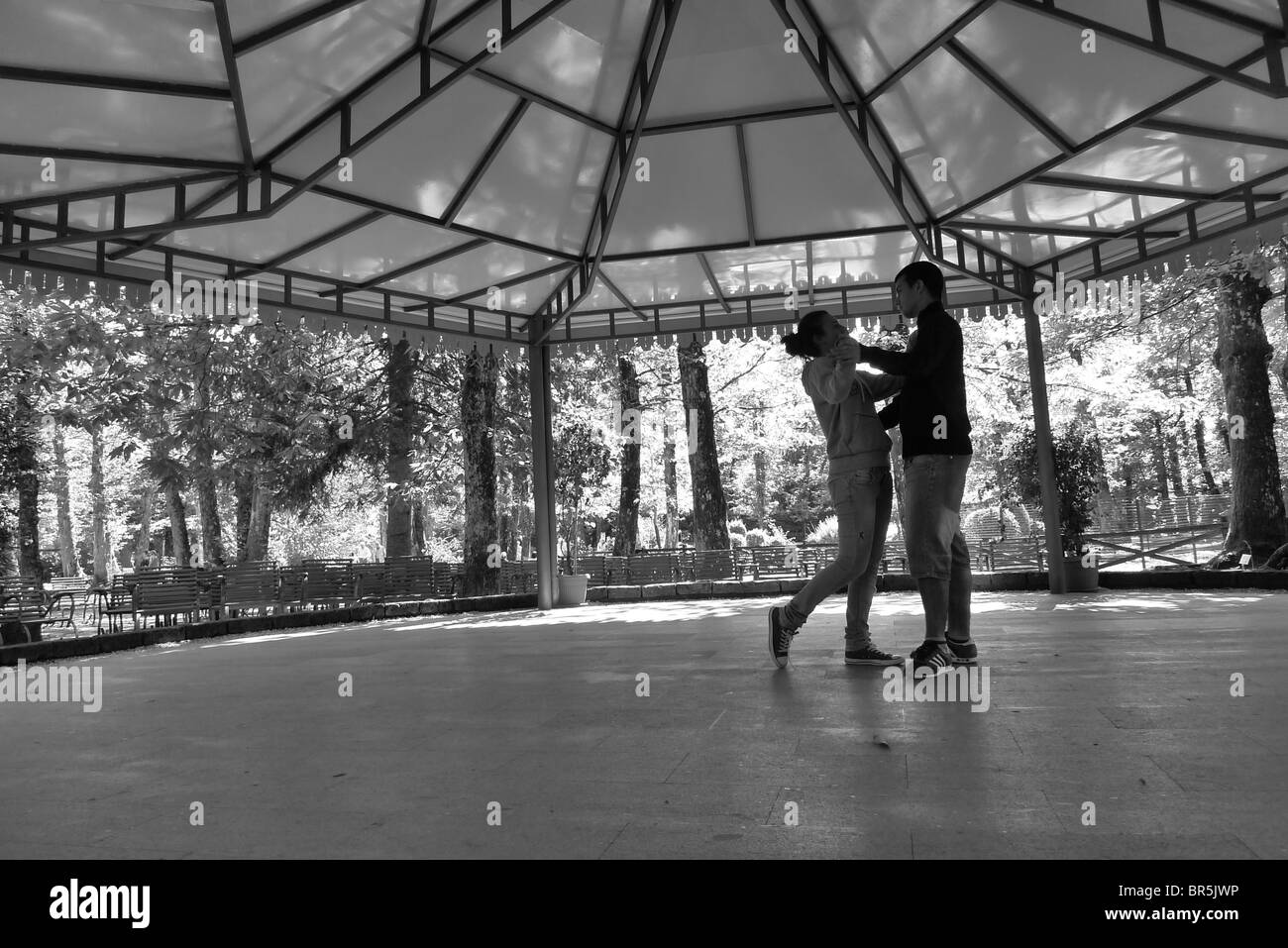 Paar von jungen und Mädchen tanzen unter einem Pavillon, Stühle und Bäume, die sie umgibt. Breiten flachen Winkel Perspektive. Stockfoto