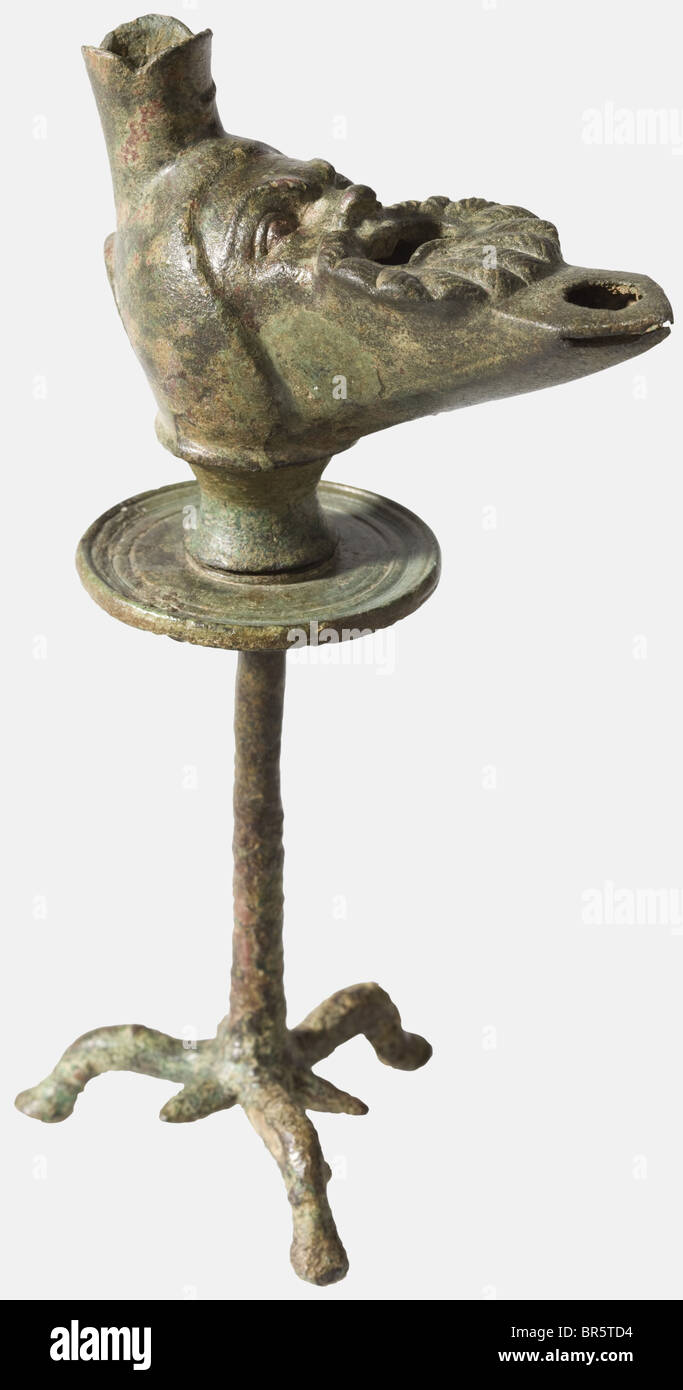 Eine römische Bronzelampe mit Stativständer, 1./2. Jahrhundert aus Bronze, ergänzt durch Kaltarbeit. Aus zwei Teilen. Die Lampe in Form einer bärtigen Comedian's Maske, der Mund - der mit Öl gefüllt war - weit offene, ausdrucksstarke Augen, die Brows und die Nase deutlich geformt. Inkl. Stativständer mit drei stilisierten, ausgestellten Tierbeinen mit genau passender Montage. Fein meißelig. Höhe 16,8 cm. Leicht gefleckte Patina, kleine Abplattung vorne am Dochloch, kleine Reparatur am Stamm. Vgl. Peter La Baume, Römische Kunstgewerbe, 1983, Stockfoto