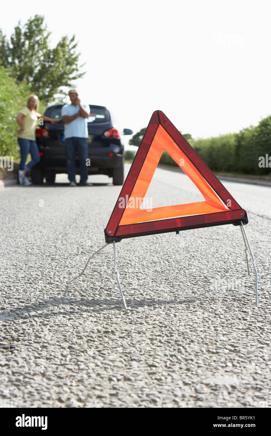 Paar Broken Down auf Landstraße mit Gefahr Warnzeichen im Vordergrund Stockfoto