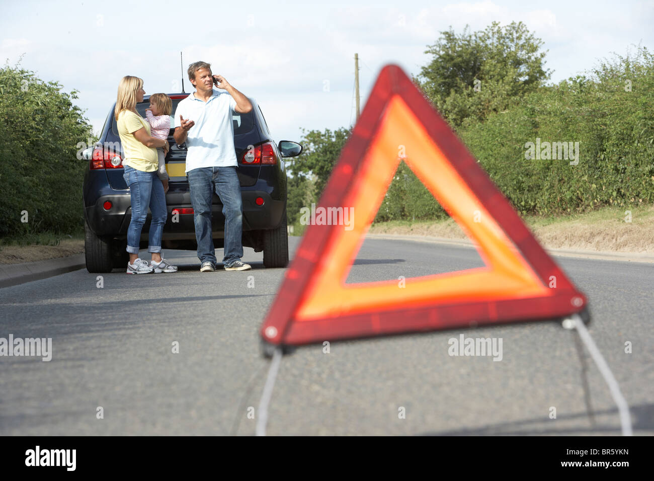 Familie Broken Down auf Landstraße mit Gefahr Warnzeichen im Vordergrund Stockfoto