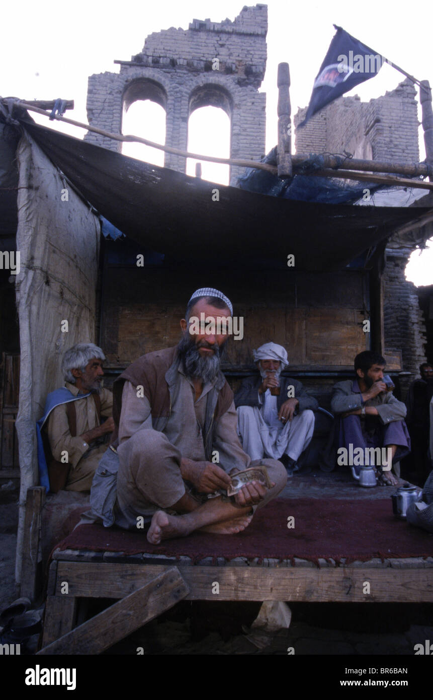 Männer trinken Tee in einem Outdoor-Tee-Shop, der sitzt unter einem zerstörten Gebäude im Stadtteil teilweise zerstörten Shor Bazar Kabul A Stockfoto