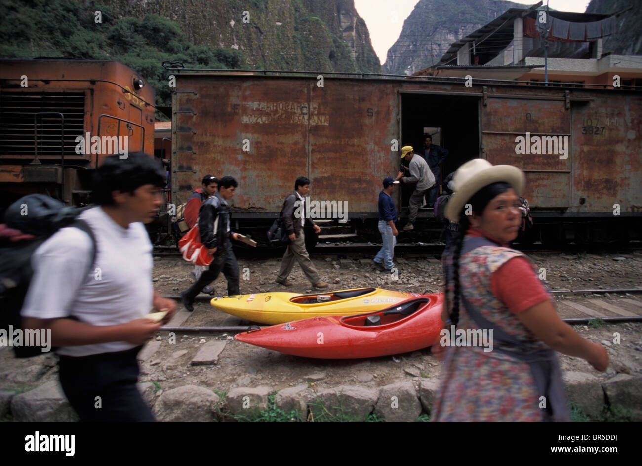Gebürtige Peruaner gehen vorbei an einem Zug und einige Kajaks in einer Stadt in der Nähe von Machu Picchu. Stockfoto