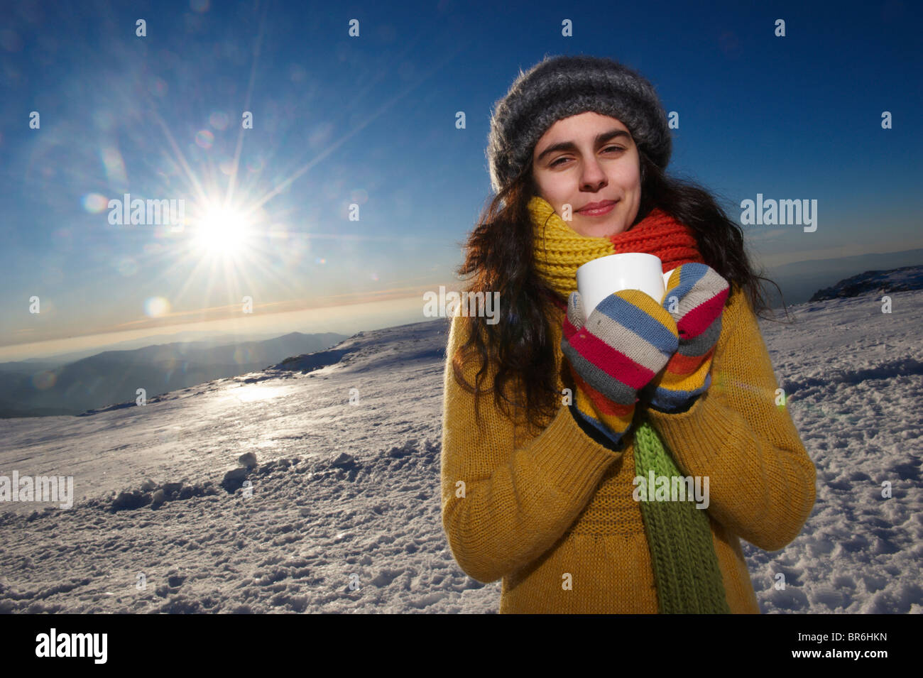 Eine lächelnde junge Frau hält eine Tasse heiße Schokolade im Schnee, Porträt Stockfoto