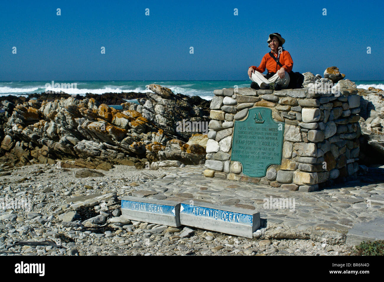 Touristen sitzen auf Denkmal am Kap Agulhas, Western Cape, Südafrika Stockfoto