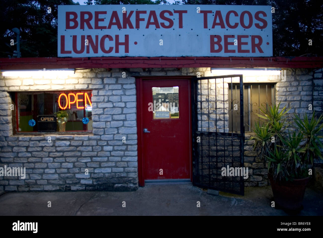 Ein Restaurant mit einer roten Tür und ein Schild in der Abenddämmerung in Bee Cave Texas. Stockfoto