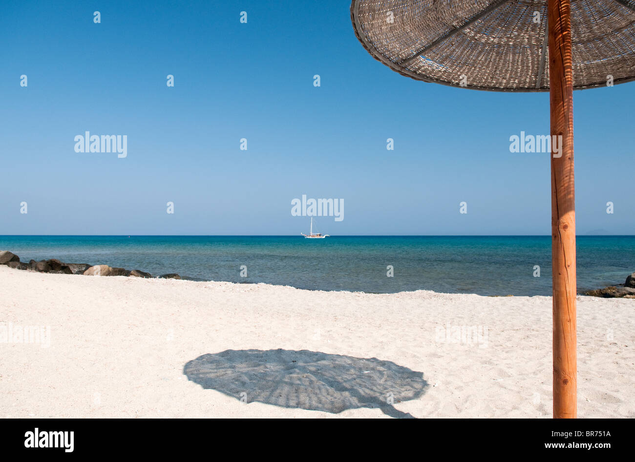 ein Sonnenschirm wirft einen Schatten an einem Strand in Griechenland Stockfoto