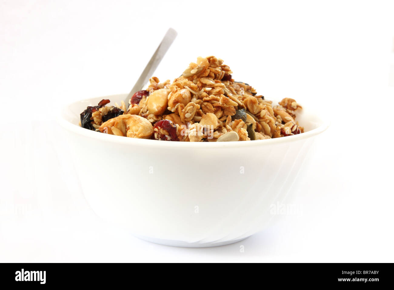 Gebackene Müsli in weiße Schüssel mit Früchten und Nüssen auf weißem Hintergrund mit einem Löffel Stockfoto