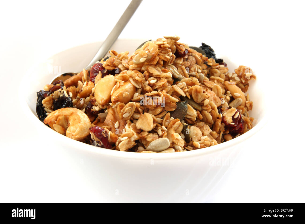 Gebackene Müsli in weiße Schüssel mit Früchten und Nüssen auf weißem Hintergrund mit einem Löffel Stockfoto