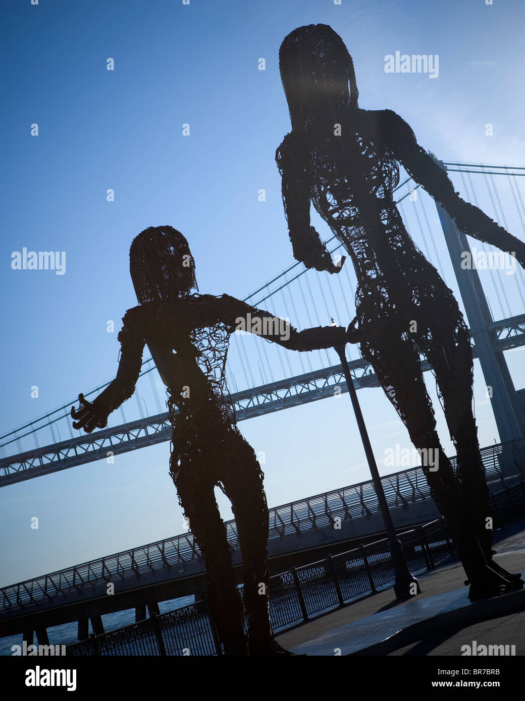 Metall-Skulptur von zwei Personen mit einer Brücke im Hintergrund. Stockfoto