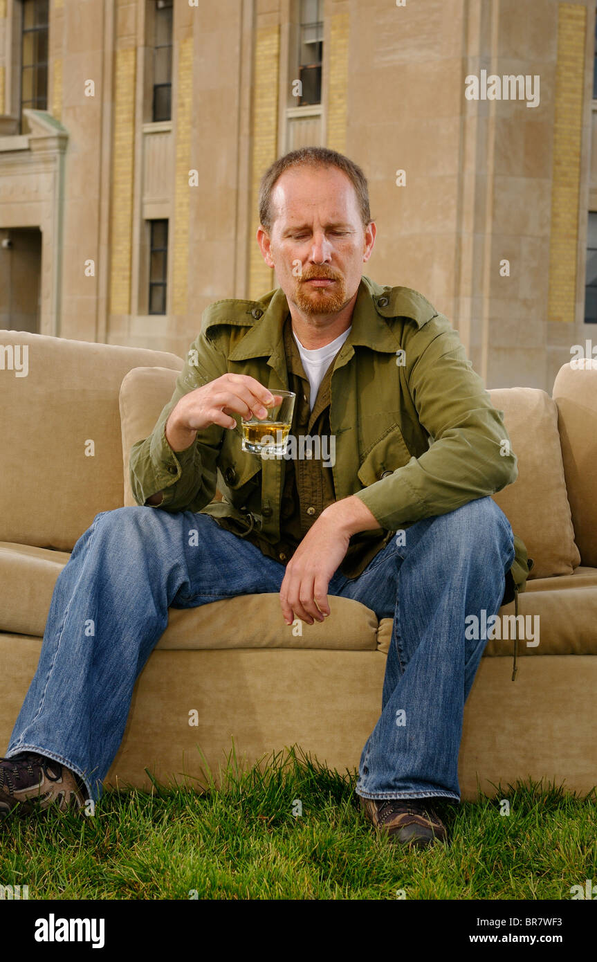 Mann sein Whiskeyglas sitzt auf einer Couch auf dem Rasen des historischen Art Deco Harris Wasseraufbereitungsanlage Gebäude Toronto argwöhnisch betrachten Stockfoto