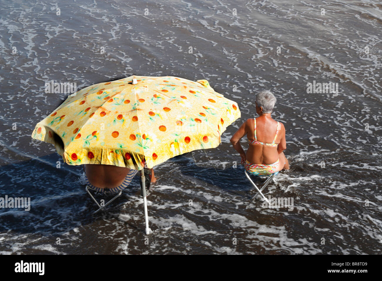Älteres paar kühl zu halten, als Wellen Runde um sie herum am Strand in Spanien Stockfoto