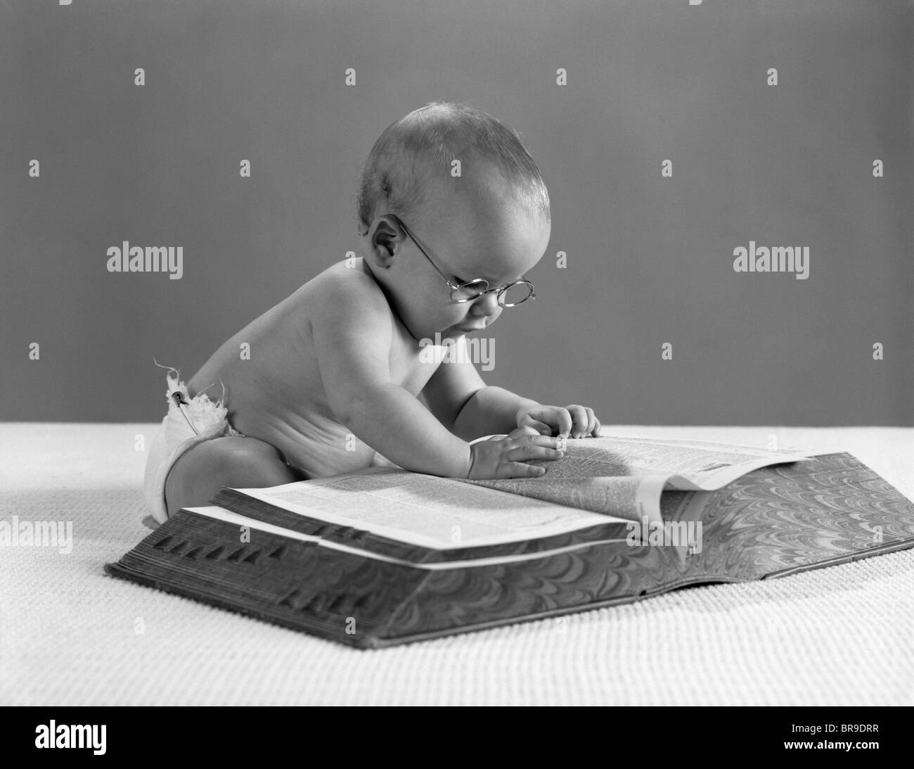 1960ER JAHREN BABY-BRILLE, DIE AUF DER SUCHE NACH EINEM WORT IN GROßES WÖRTERBUCH Stockfoto
