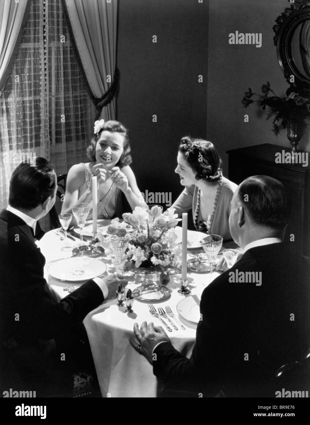1930ER JAHREN ZWEI PAARE FÖRMLICHEN DINNER-PARTY, DIE AM TISCH SITZEN Stockfoto