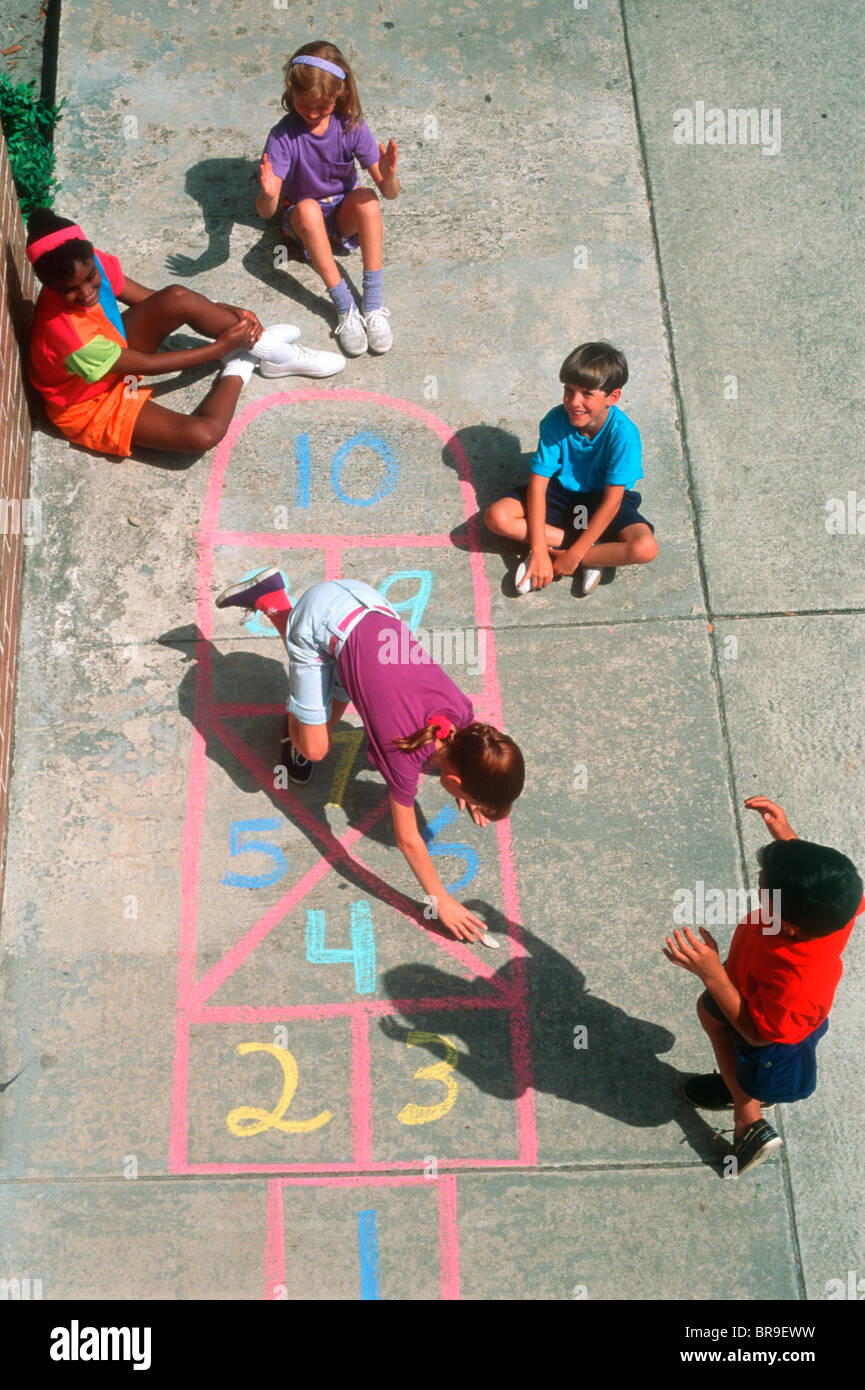 1980ER JAHRE GRUPPE VON FÜNF KINDERN, JUNGEN UND MÄDCHEN SPIELEN HOPSCOTCH AUF KONKRETE BÜRGERSTEIG Stockfoto