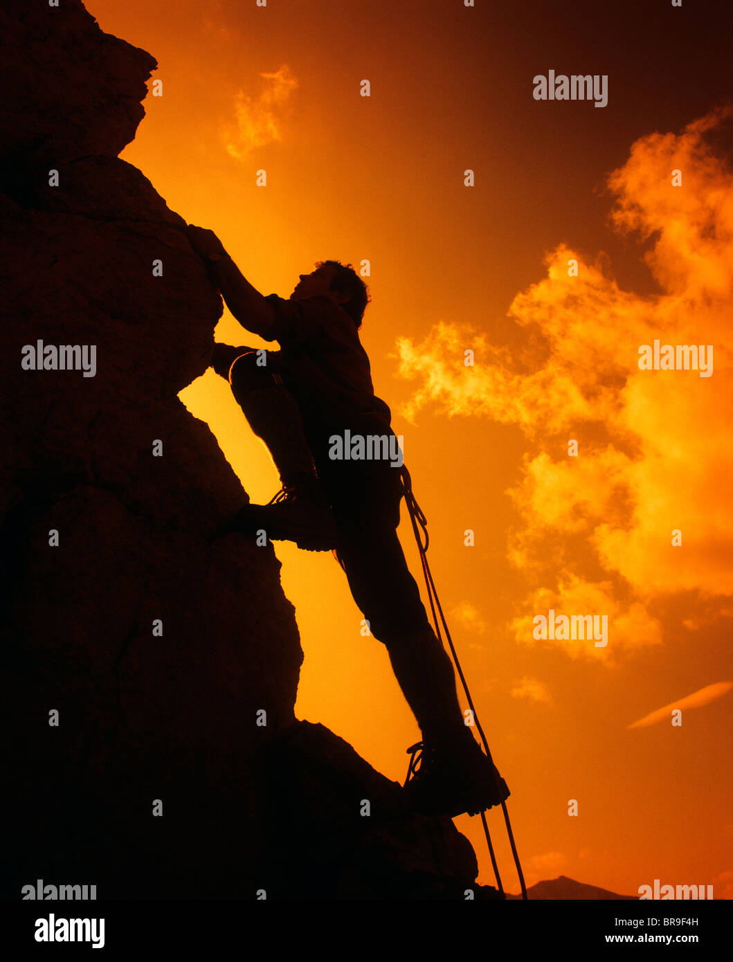 SILHOUETTE DER MANN KLETTERN GEGEN SONNENUNTERGANG HIMMEL Stockfoto