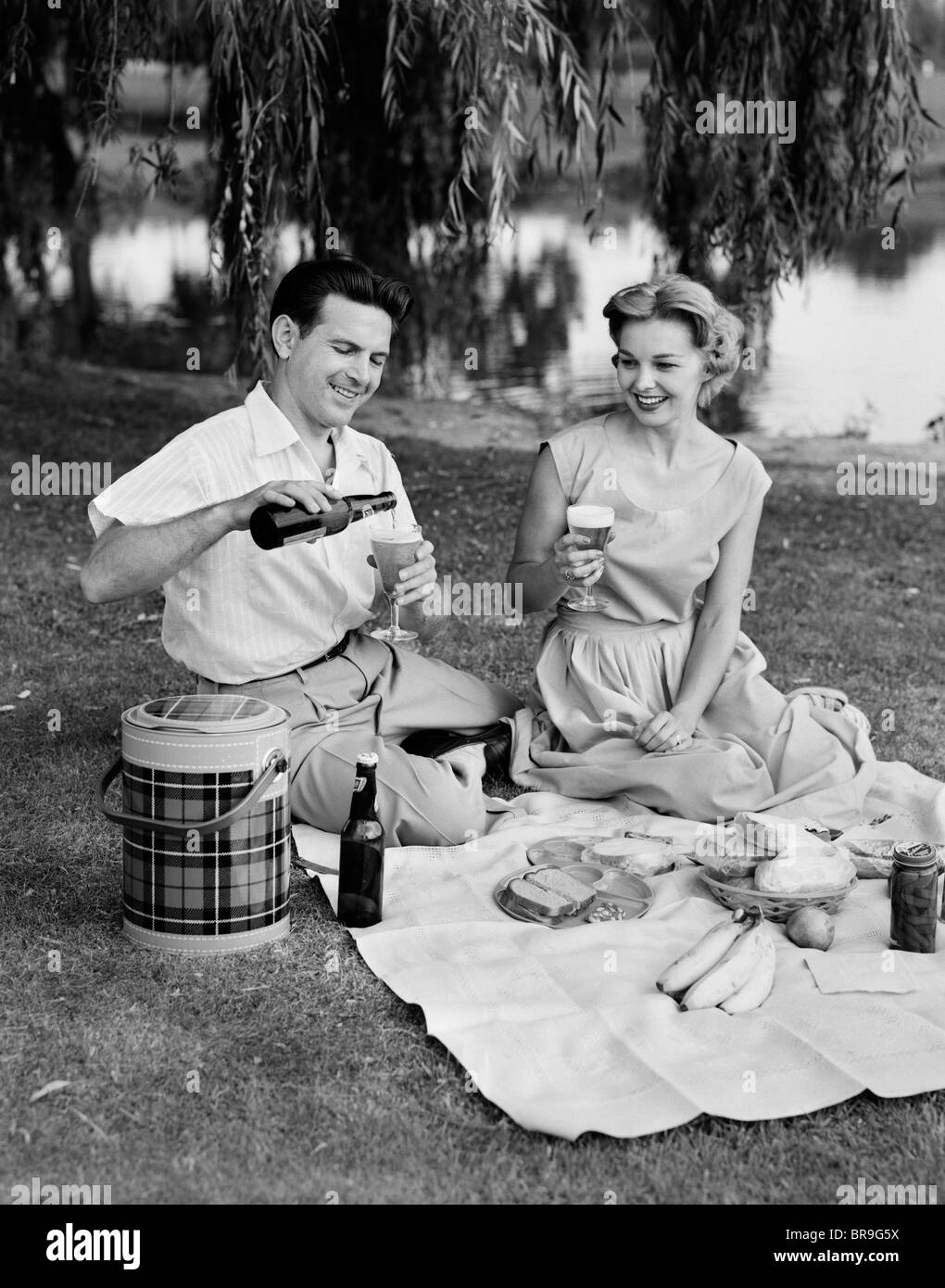 1950ER JAHRE MANN FRAU PAAR SOMMER PICKNICK IM FREIEN TRINKEN BIER Stockfoto