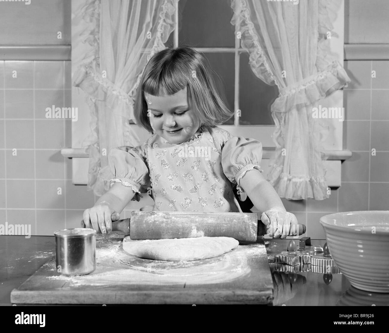 1950ER JAHREN LÄCHELND MÄDCHEN ROLLEN TEIG MEHL BACKEN IN KÜCHE Stockfoto