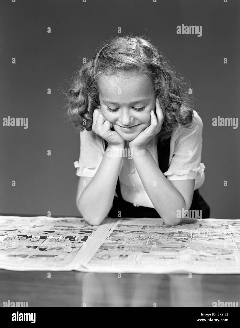 1940ER JAHRE KIND LESEN ZEITUNG COMICS LÄCHELND Stockfoto