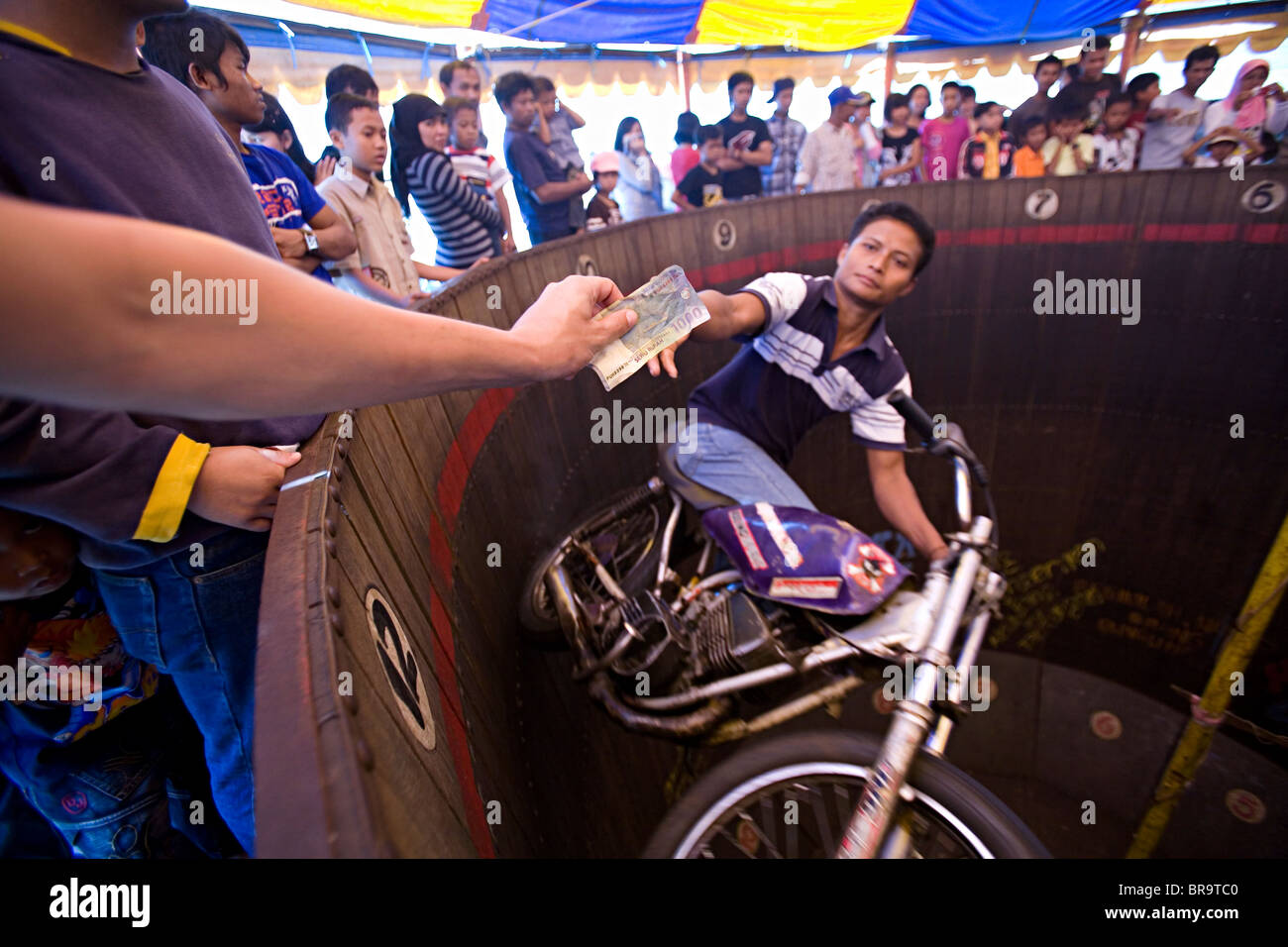 Ausgestreckter Arm halten Geld wartet, während Mann Motorrad eine Wand fährt um sie zu ergreifen. Stockfoto